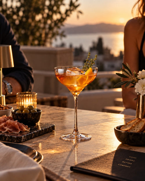 Coupette en cristal à pied long garnie d'un cocktail ambré, sur une terrasse au coucher du soleil